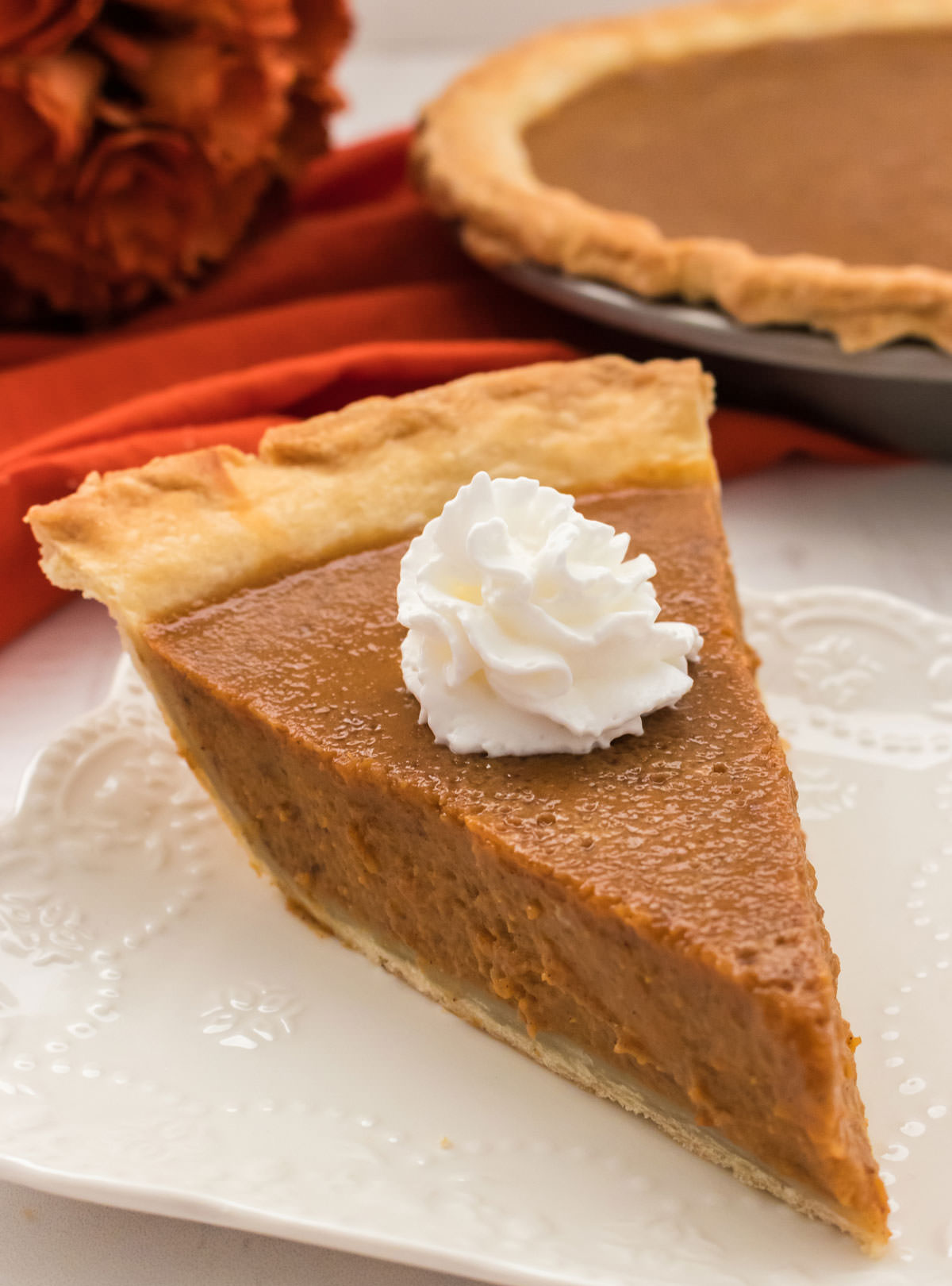 A piece of Homemade Sweet Potato Pie with a dollop of Whipped Cream sitting on a white plate.  