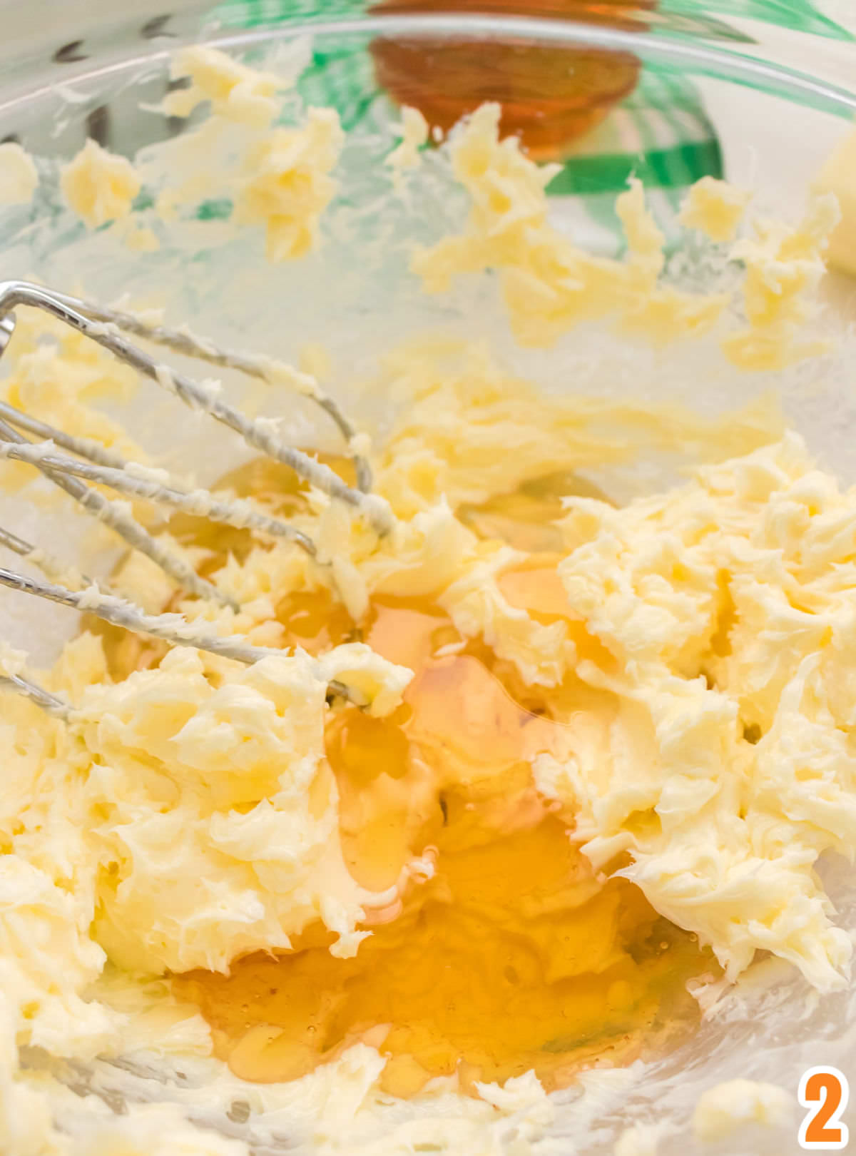 Closeup on a clear glass bowl filled with whipped butter, covered with honey and electric beaters.