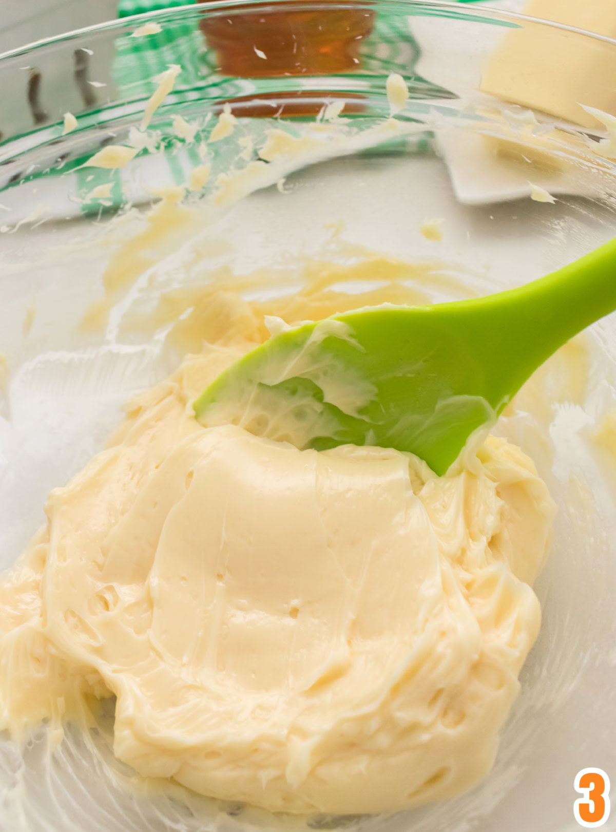 Closeup on a clear glass bowl filled with honey butter and a green spatula.