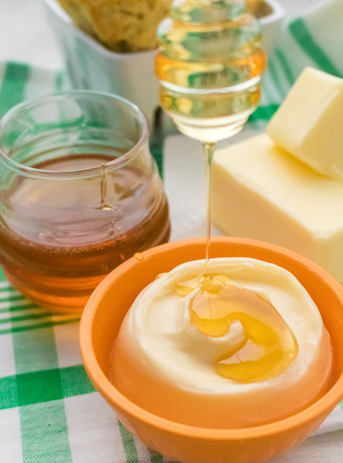 Closeup on a orange ramekin filled with Honey Butter with honey dripping down on to the honey.