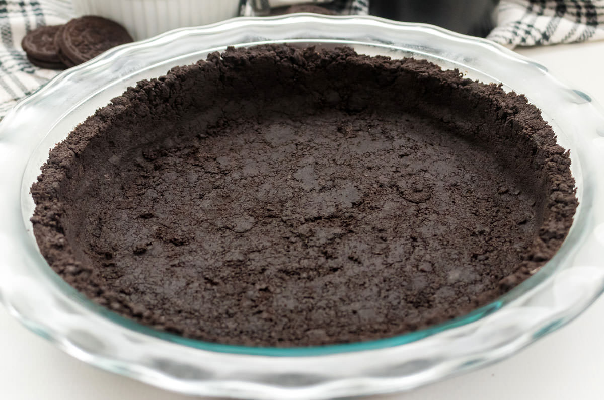 Closeup on an Oreo Cookie Pie Crust in a clear glass Pie Plate sitting on a white surface.