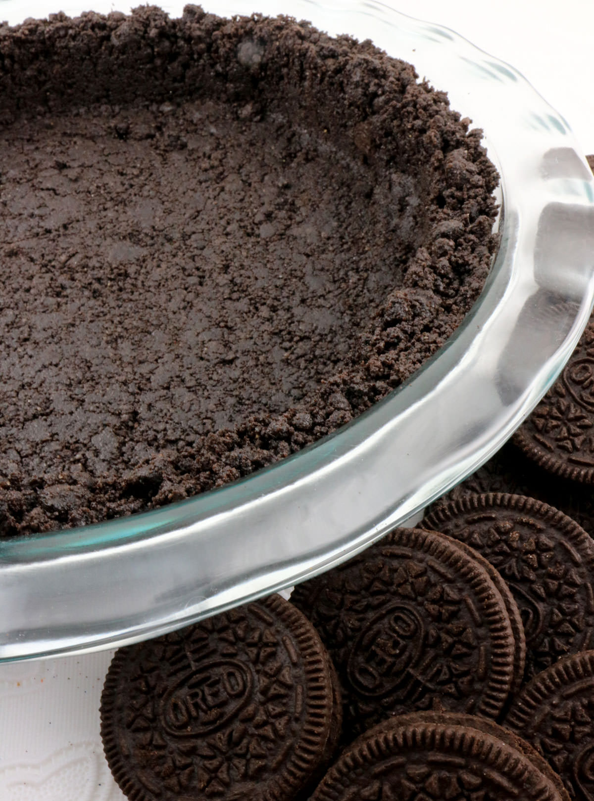 Closeup on an Oreo Cookie Pie Crust in a glass pie pan surrounded by Oreo Cookies.