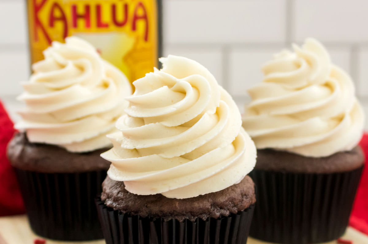 Closeup on three cupcakes topped with Kahlua Buttercream Frosting sitting in front of a bottle of Kahlua Rum and Coffee Liqueur.