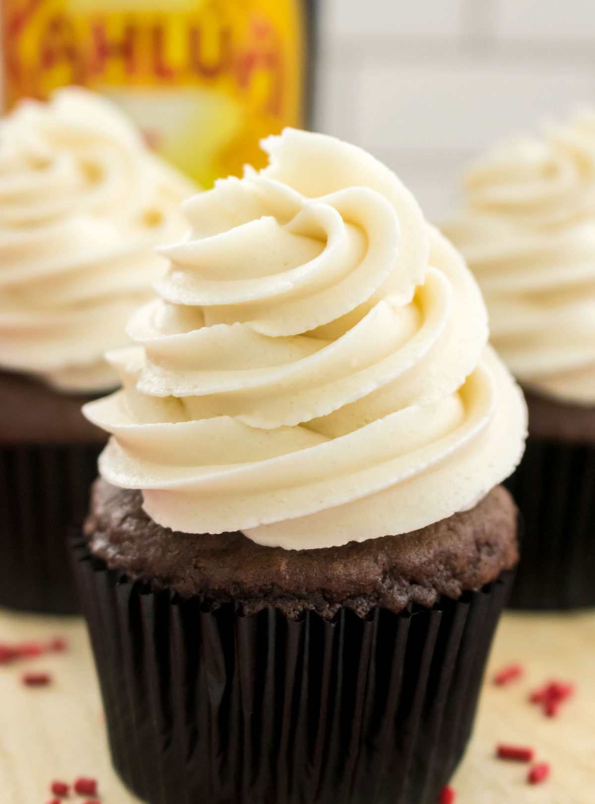Closeup on a chocolate cupcake frosted with Kahlua Buttercream Frosting sitting on a cutting board in front of a bottle of Kahlua Rum and Coffee Liqueur.