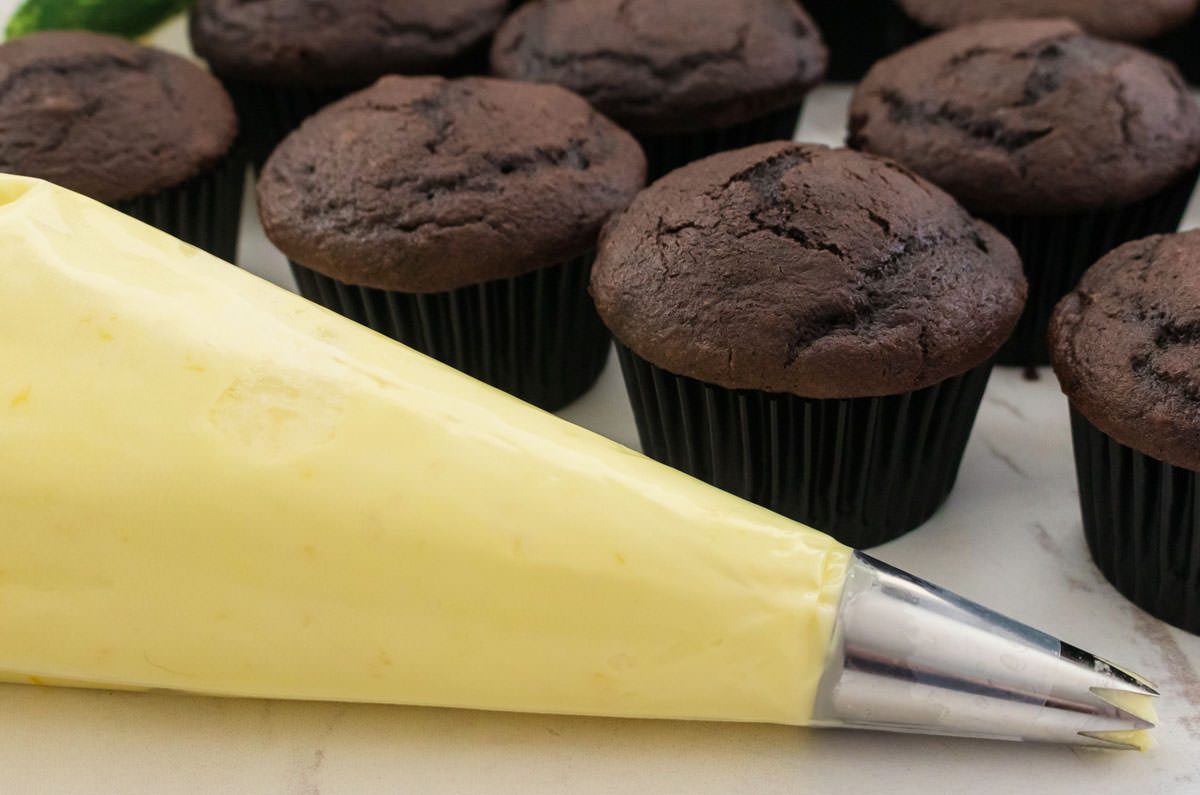 Closeup on a decorating bag filled with Lemon Frosting sitting in front of a batch of unfrosted chocolate frosting.