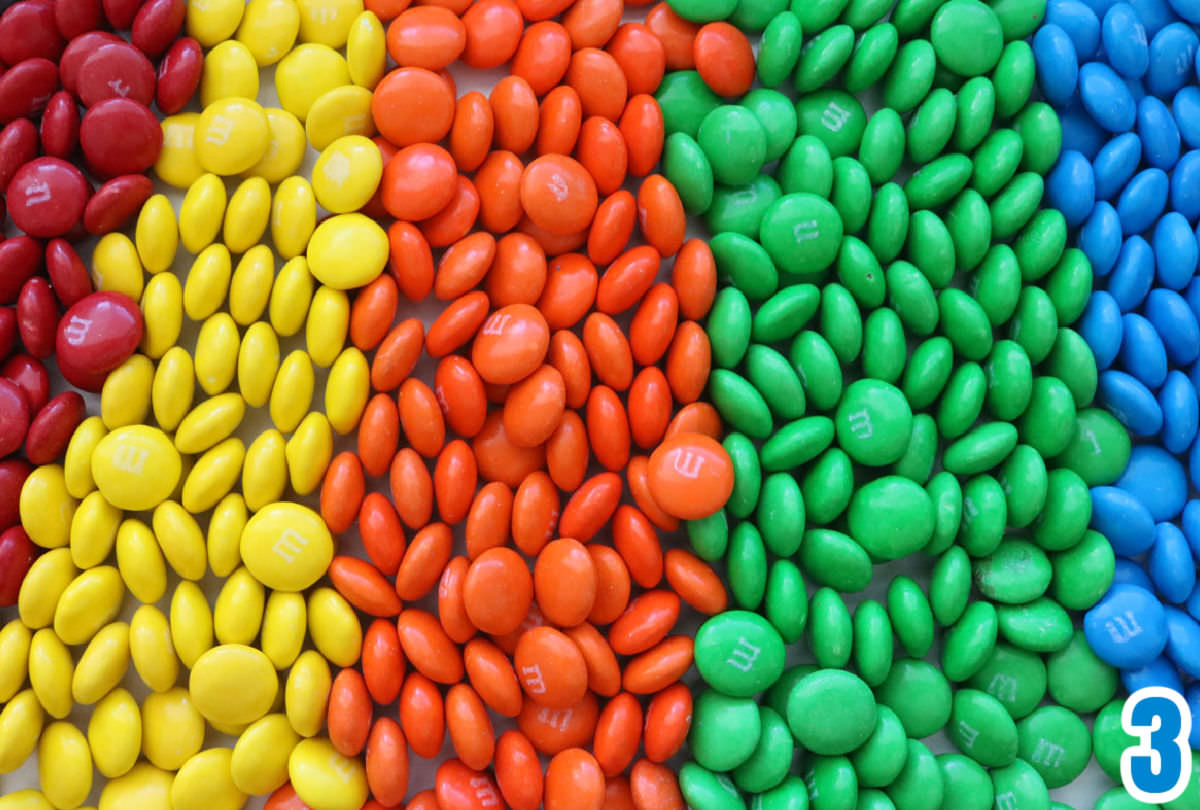 M&M's arranged in a rainbow pattern on a white surface.