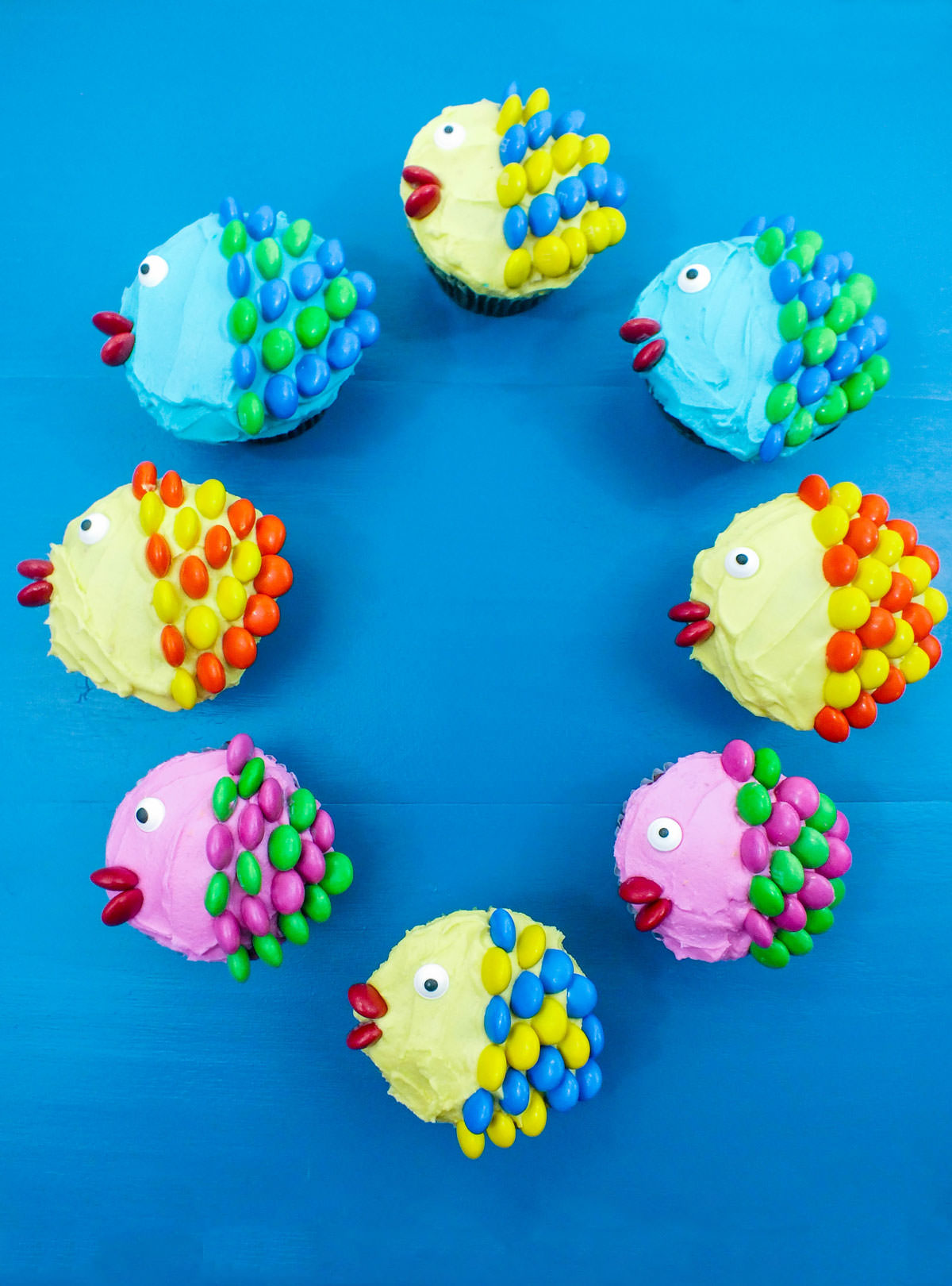 Eight Little Fishy Cupcakes arranged in a circle on a blue surface.