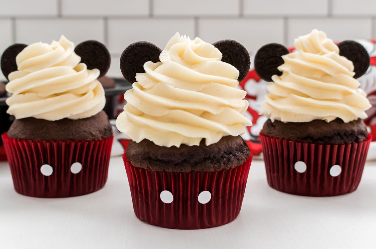 Closeup on three Mickey Mouse Cupcakes with buttercream frosting and red cupcake liners and oreo ears.