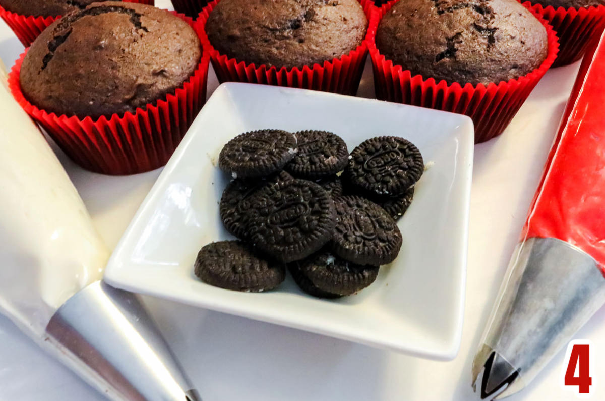 White ramekin filled with Mini Oreos surrounded by decorating bags filled with frosting and chocolate cupcakes.