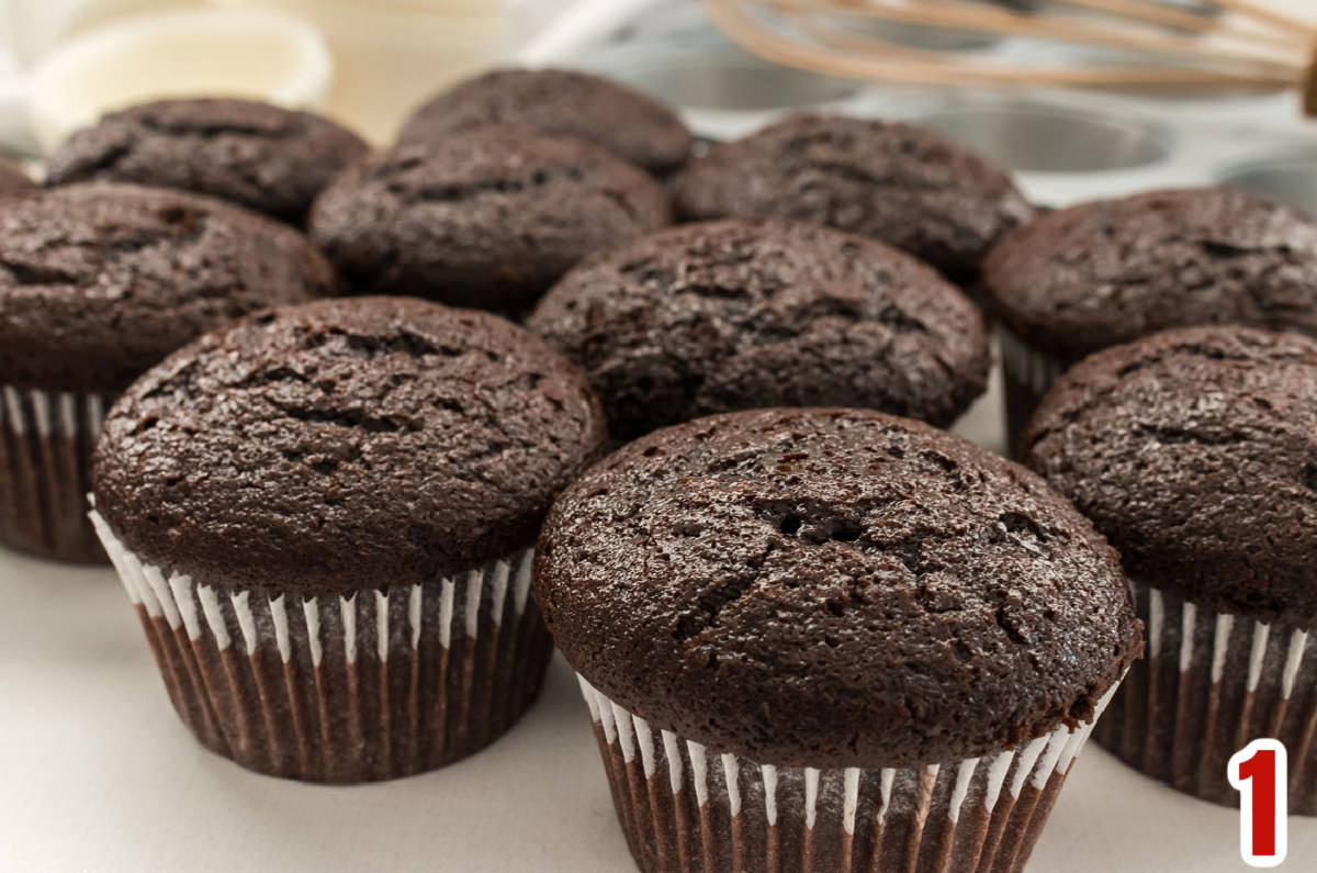 A dozen unfrosted chocolate cupcakes sitting on a white table.