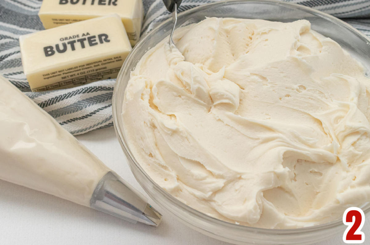 Closeup on a glass bowl filled with homemade buttercream frosting sitting next to a decorating bag filled with frosting.