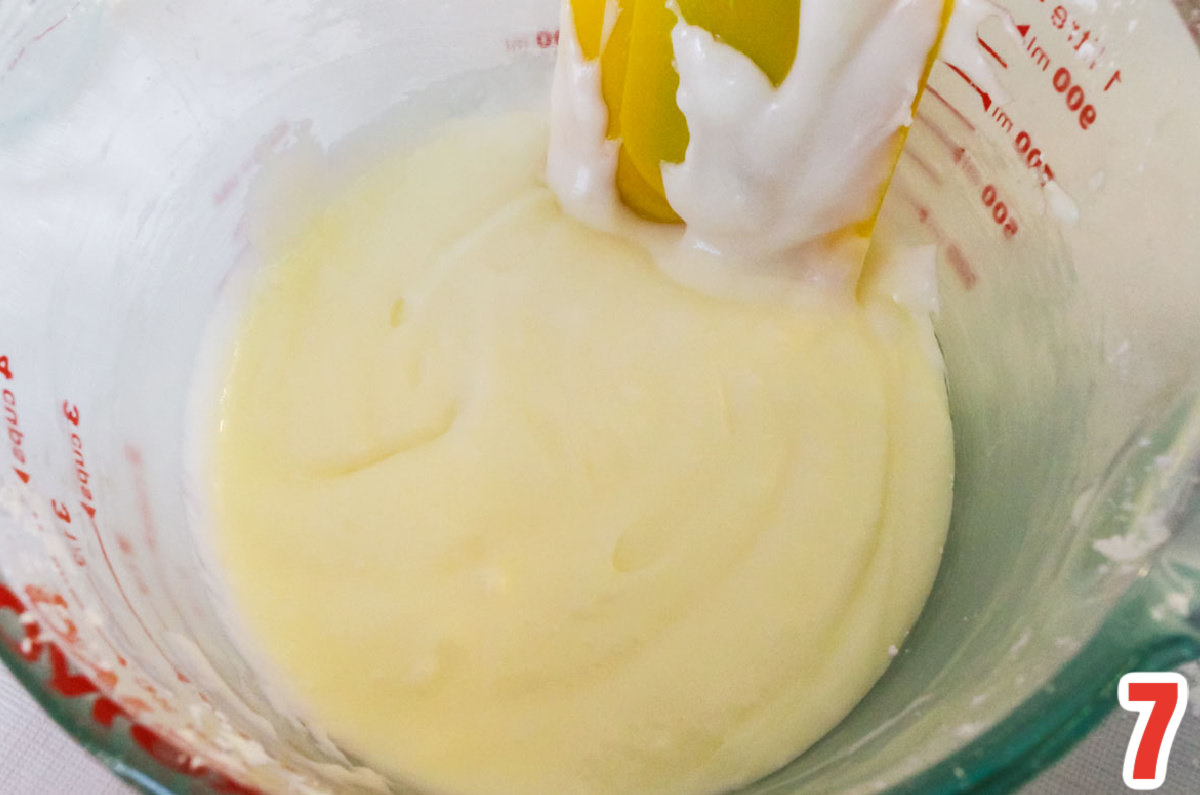 Closeup on a large glass measuring cup filled with the cake icing and a spatula.