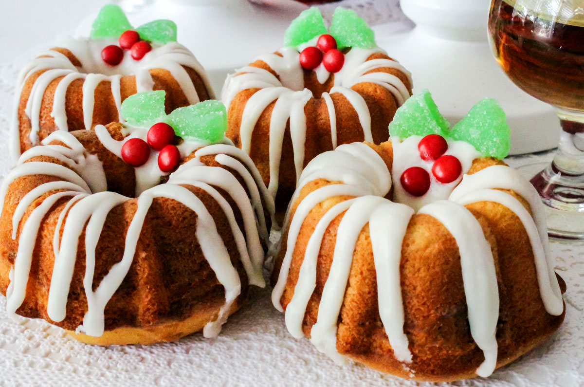 Closeup on four Christmas Mini Bundt Cakes sitting on a white table next to a glass of Sherry.