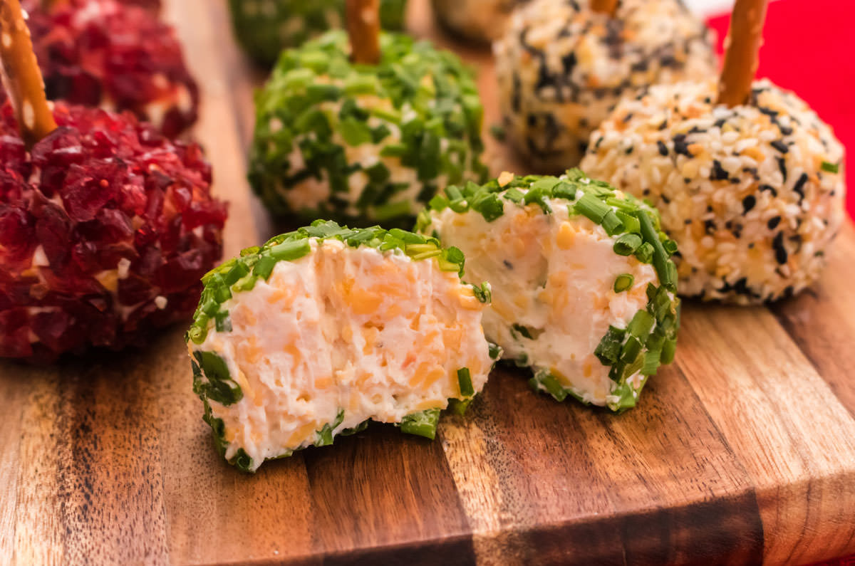 Close up of Cheese Ball Bites on a cutting board with one cut in half to showing the cheese filling.