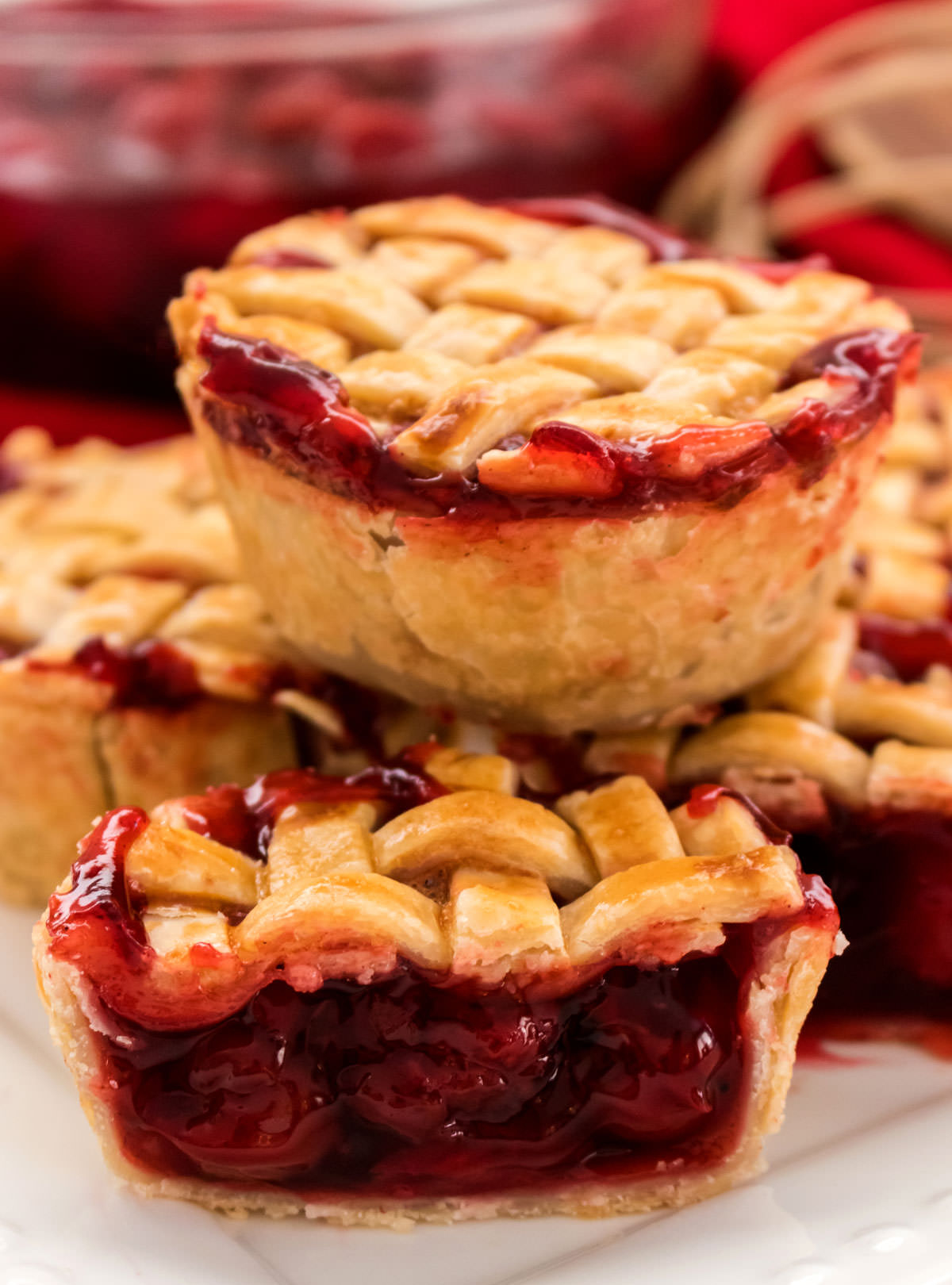 Closeup on a stack of Mini Cherry Pies sitting on a white plate, one of the Mini Pies is cut in half so you can see the Cherry Filling inside.
