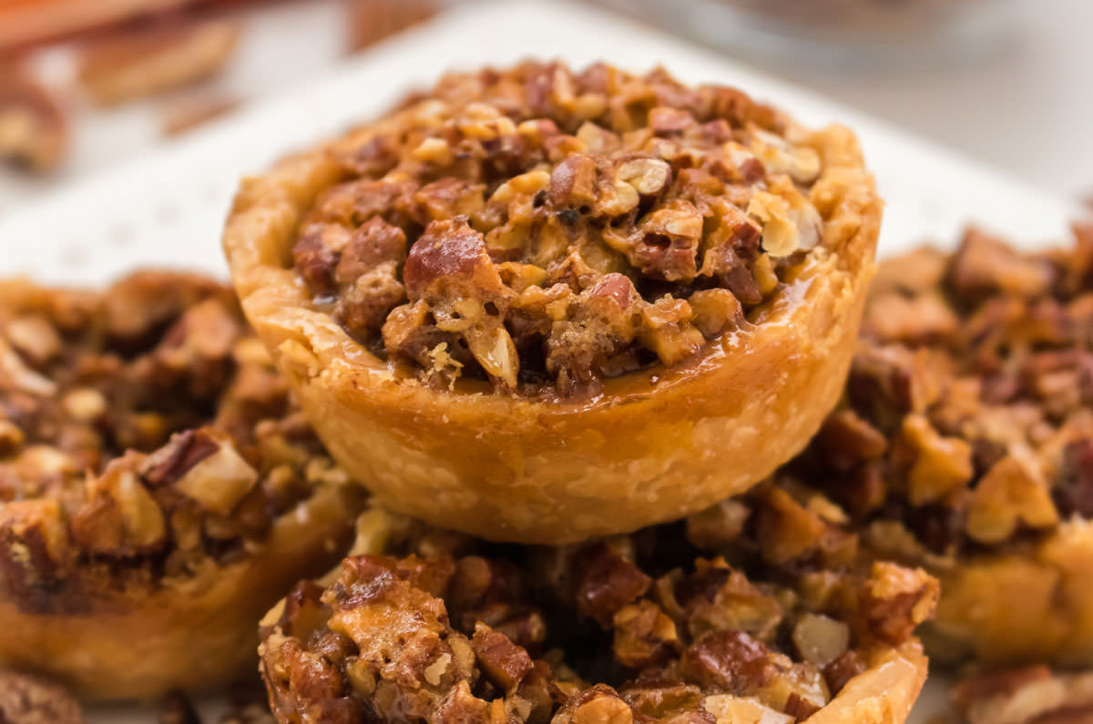 Closeup on a Mini Pecan Pie sitting atop a stack of mini pies on a white plate.