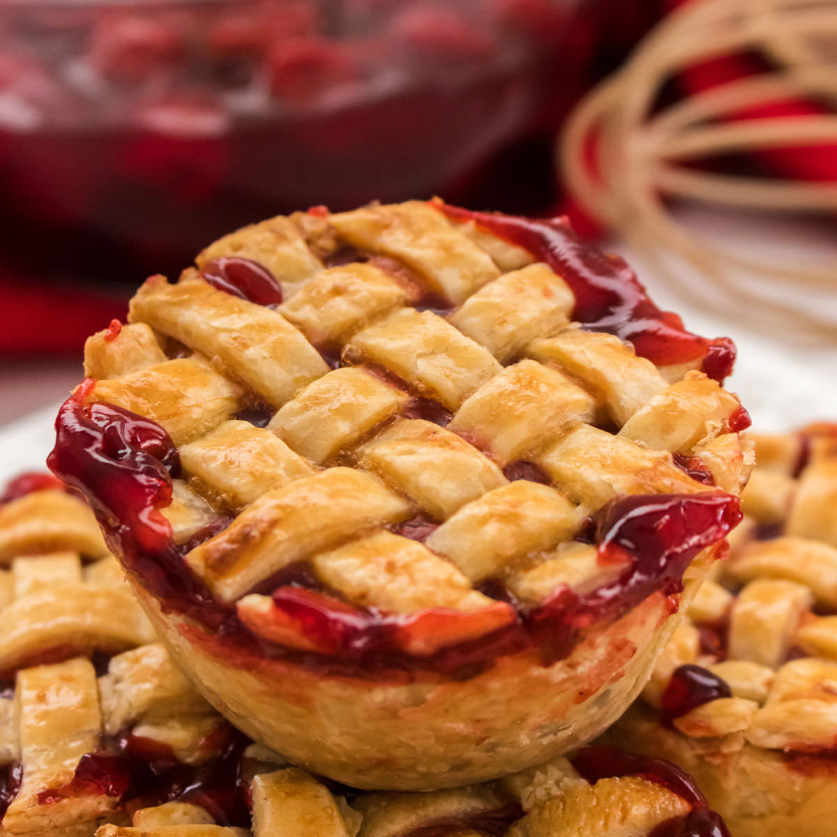 Closeup on a Mini Cherry Pie with a lattice pie crust top sitting on a pile of other pies.