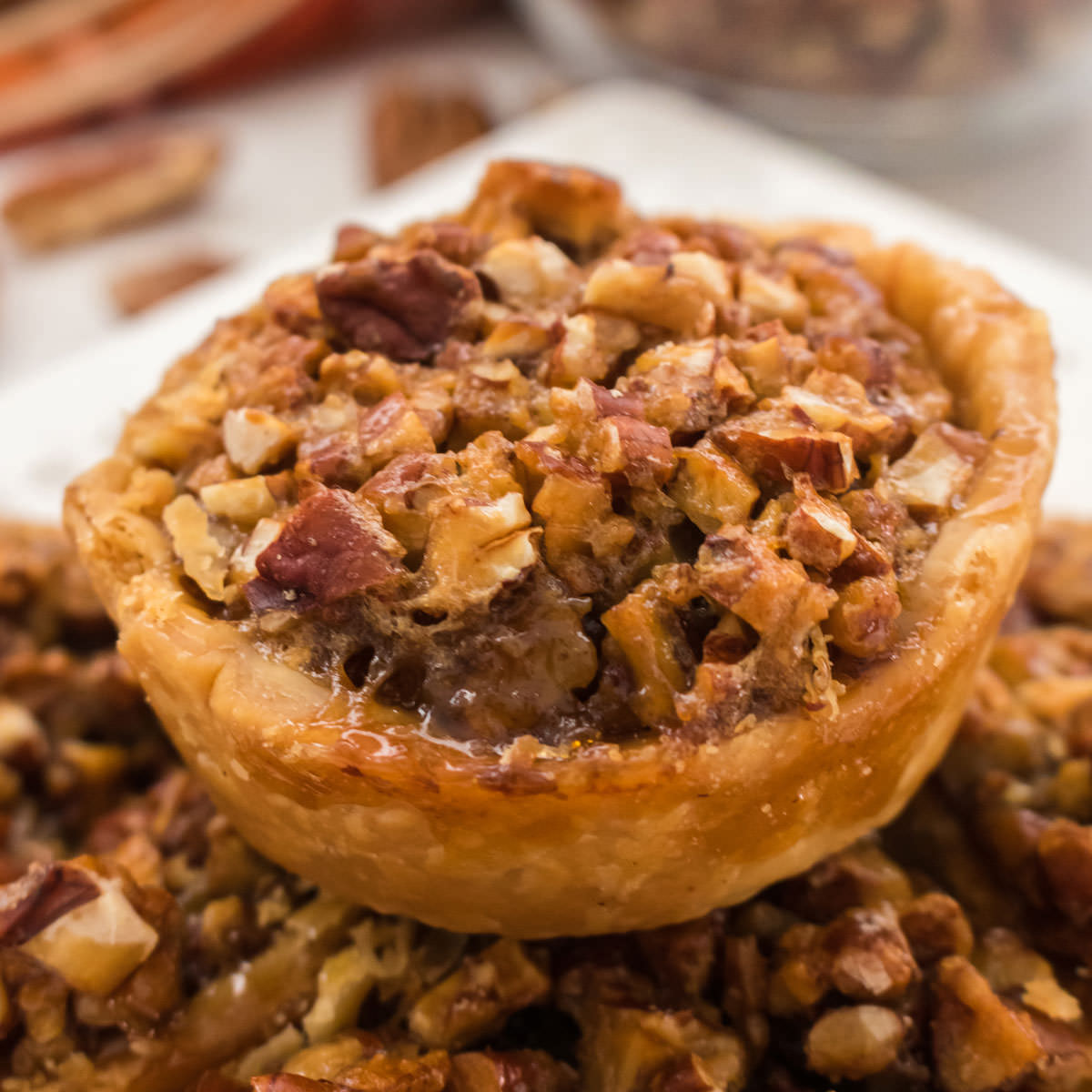 Closeup on a Mini Pecan Pie sitting on a stack of other pies on a white plate.