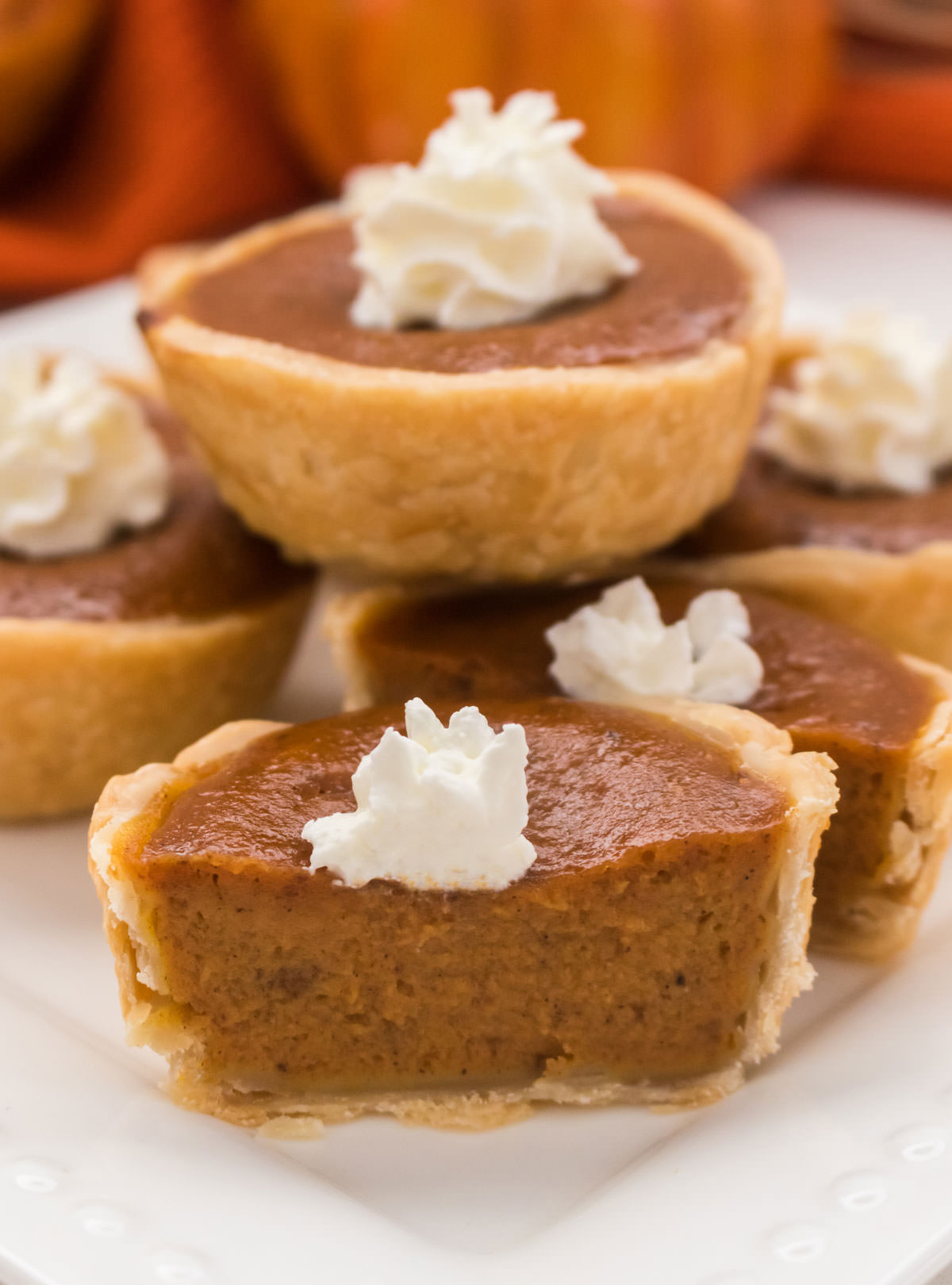Closeup on five Mini Pumpkin Pies sitting on a white plate, one of which is cut in half so you can see the Pumpkin Filling.
