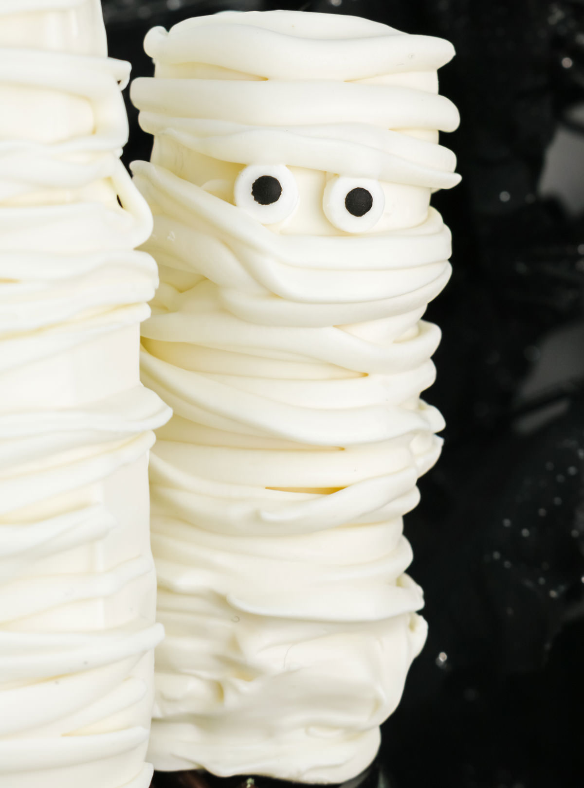 Closeup of a Mummy Marshmallow Pop standing up in front of a spooky black background.