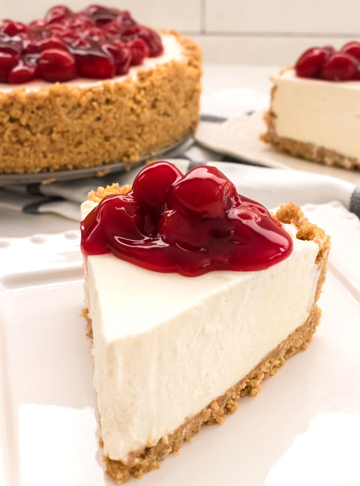 Close up of a piece of No Bake Cheesecake sitting on a white plate in front of the rest of the cheese cake.