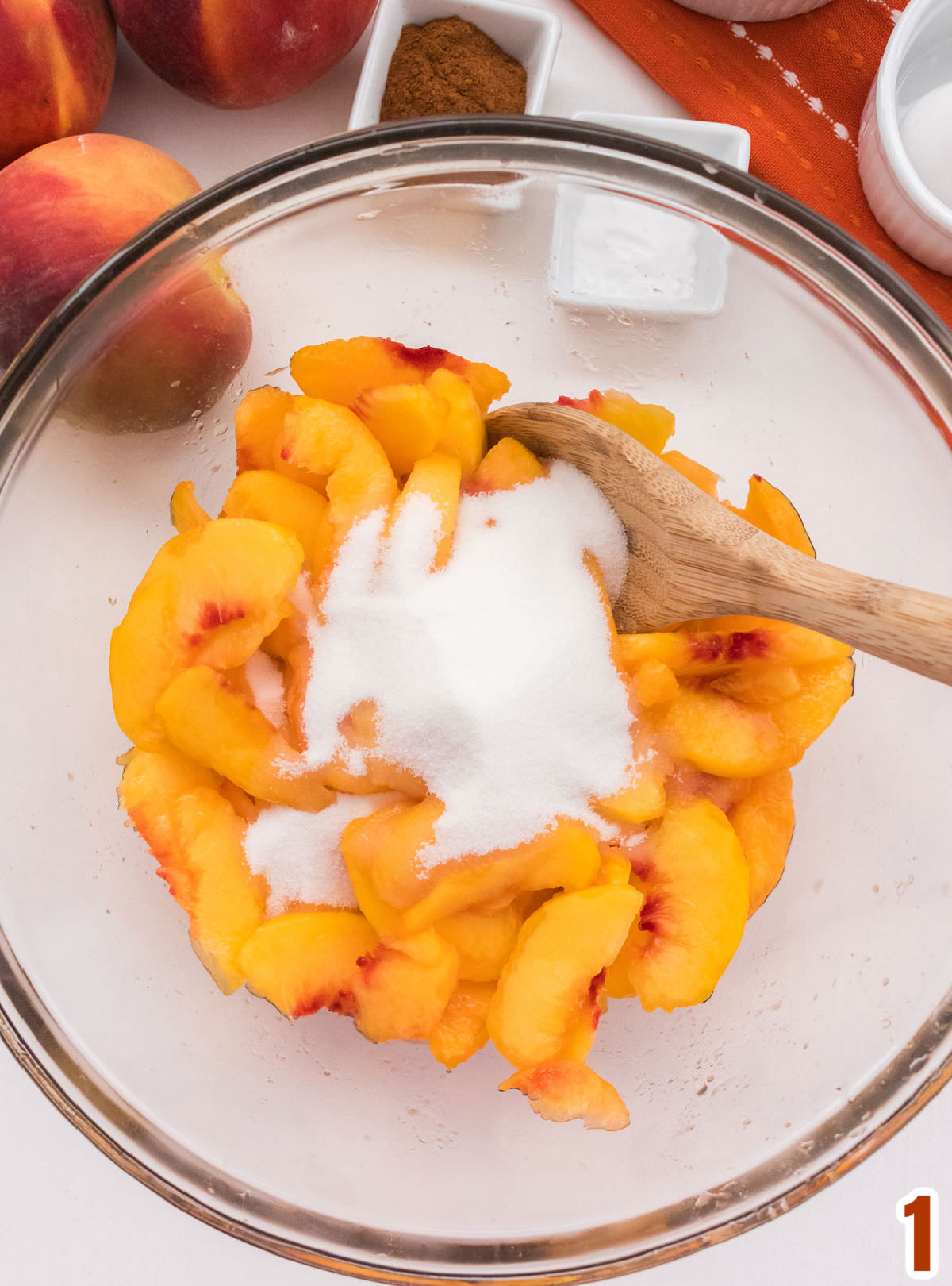 Closeup on a clear glass bowl filled with Peeled and Sliced fresh peaches covered with sugar.