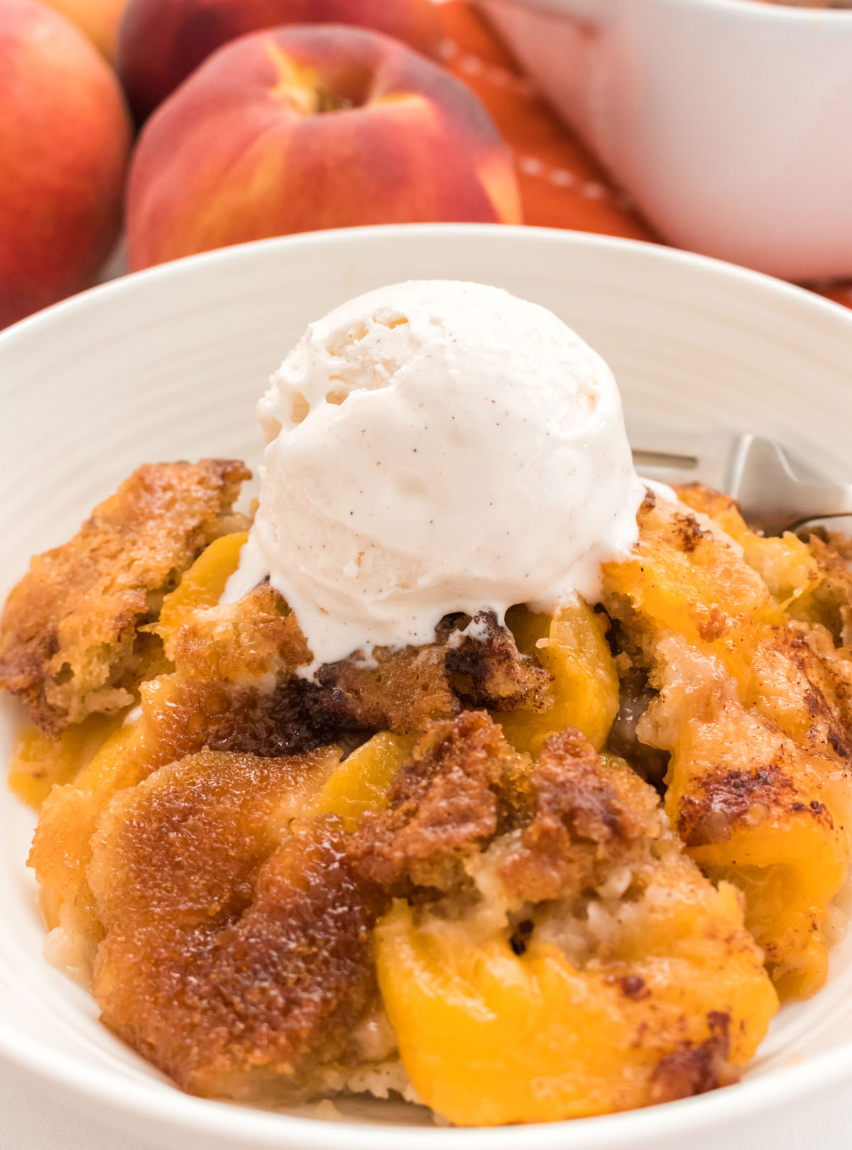 Closeup on a white bowl filled with warm Old Fashioned Peach Cobbler topped with a scoop of vanilla ice cream.