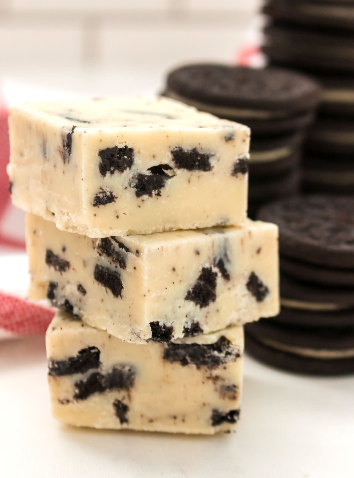 Three pieces of Oreo Fudge sitting on a white table next to a stack of Oreo Cookies.