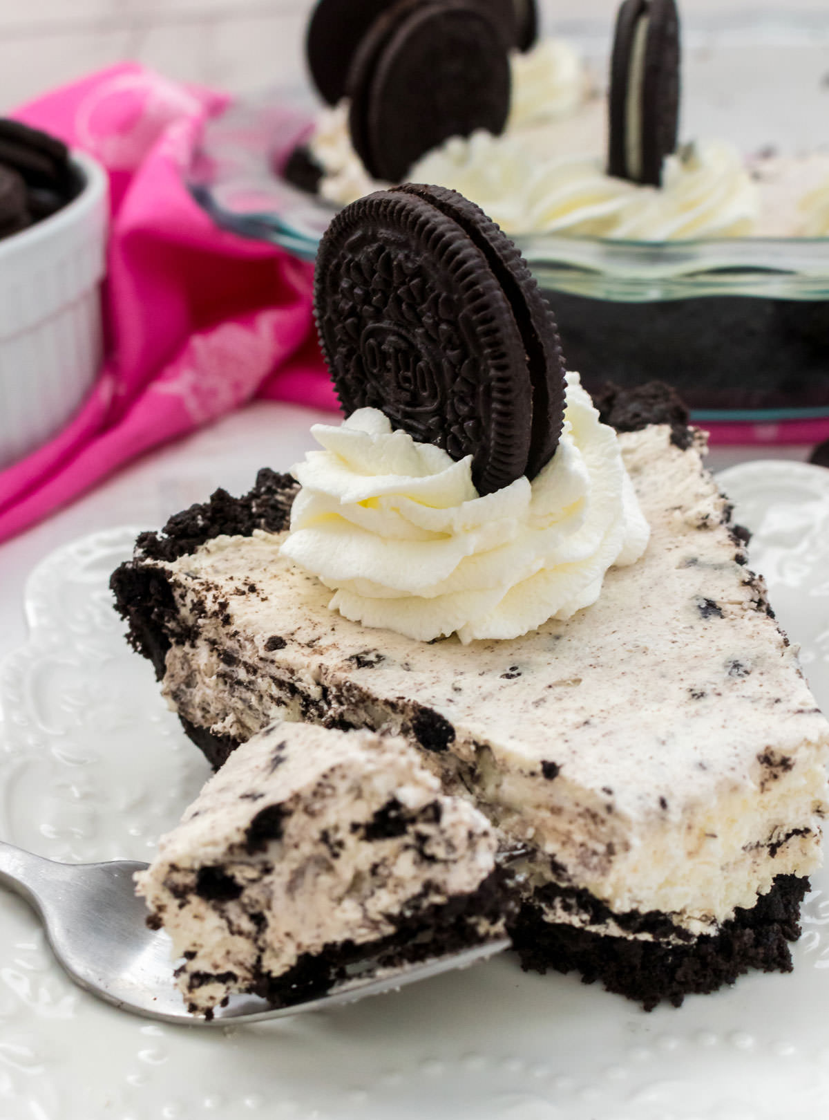 Closeup on a single piece of No Bake Oreo Cream Pie sitting on a white plate in front of the rest of the pie.