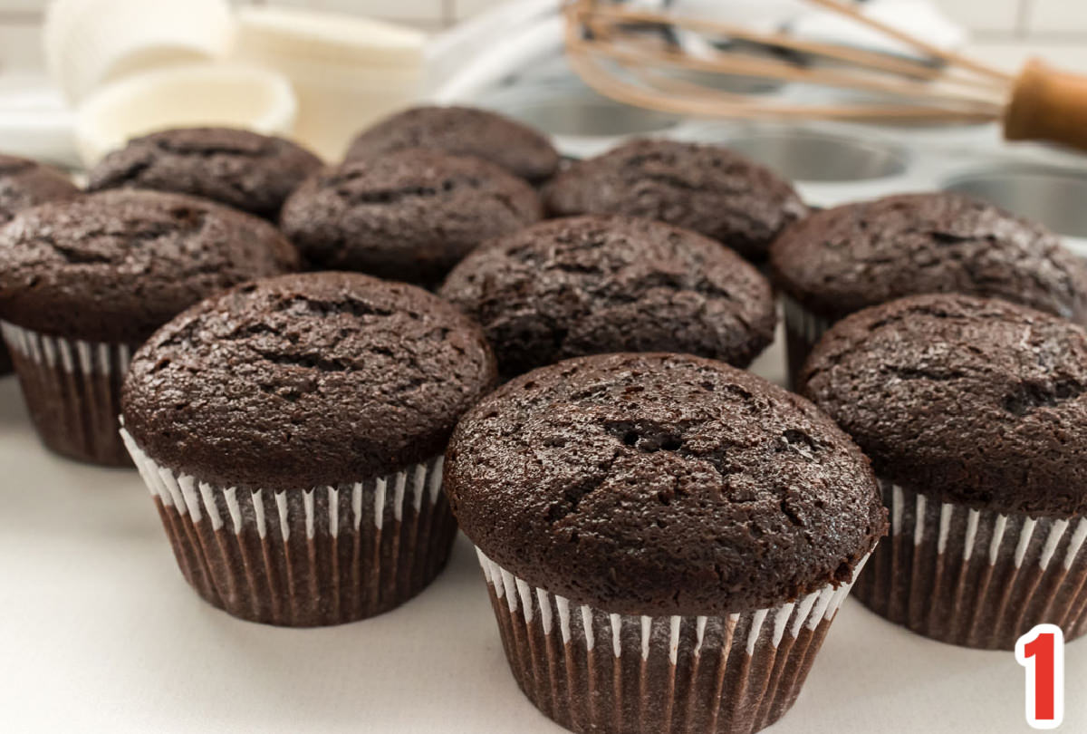 Closeup of a dozen chocolate cupcakes in white cupcake liners on a white table.