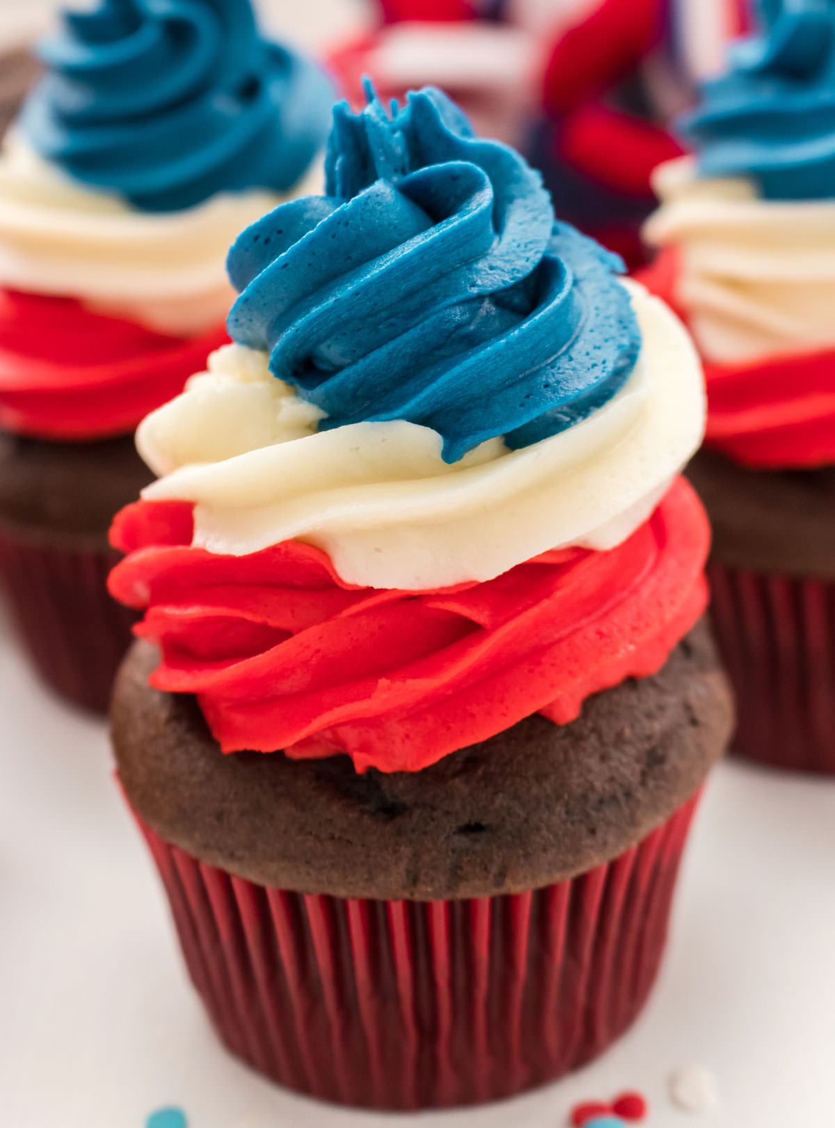 Closeup of a Patriotic Swirl Cupcake with Red White and Blue Buttercream Frosting sitting in front of other 4th of July cupcakes.