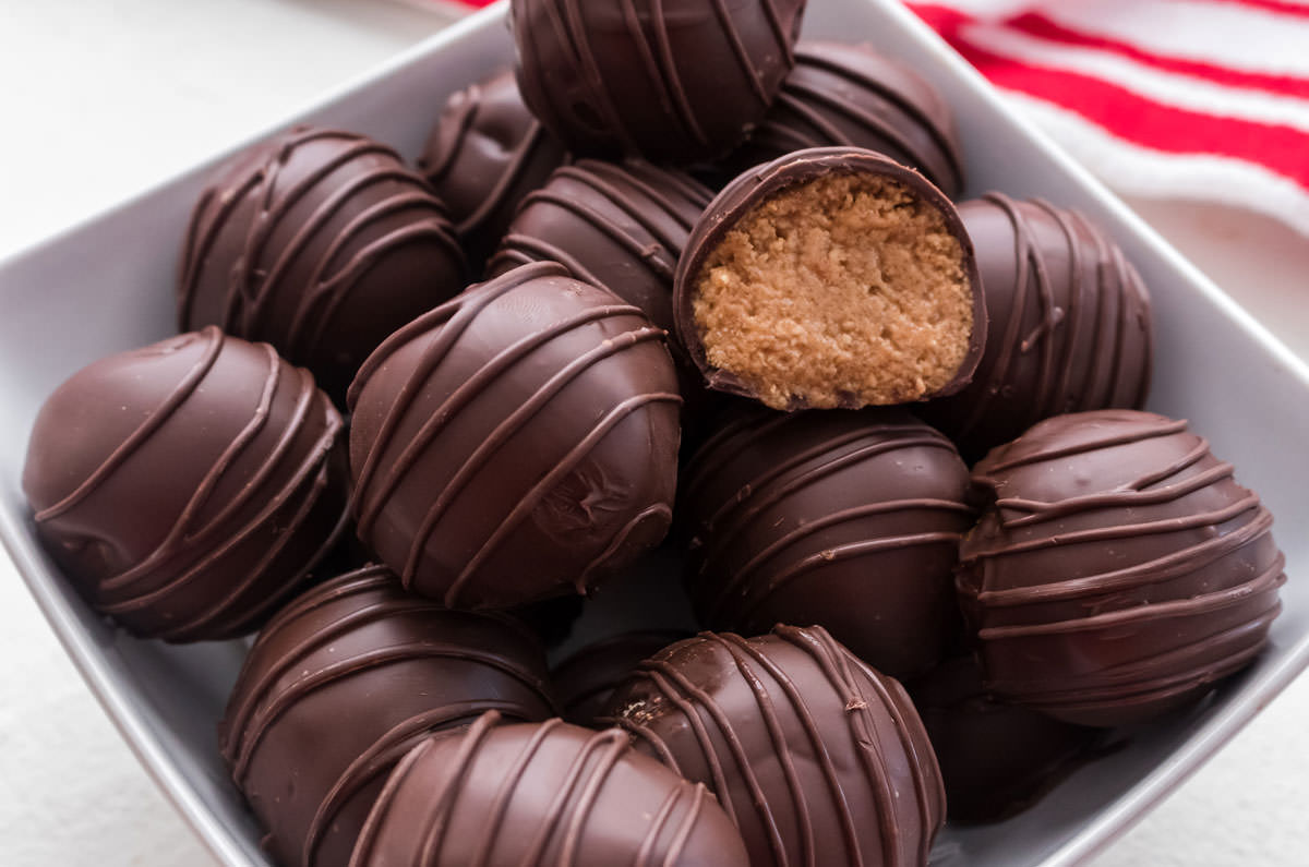 Close up of a white bowl filled with Peanut Butter Candies including one candy that is cut in half to showing the peanut butter filling.