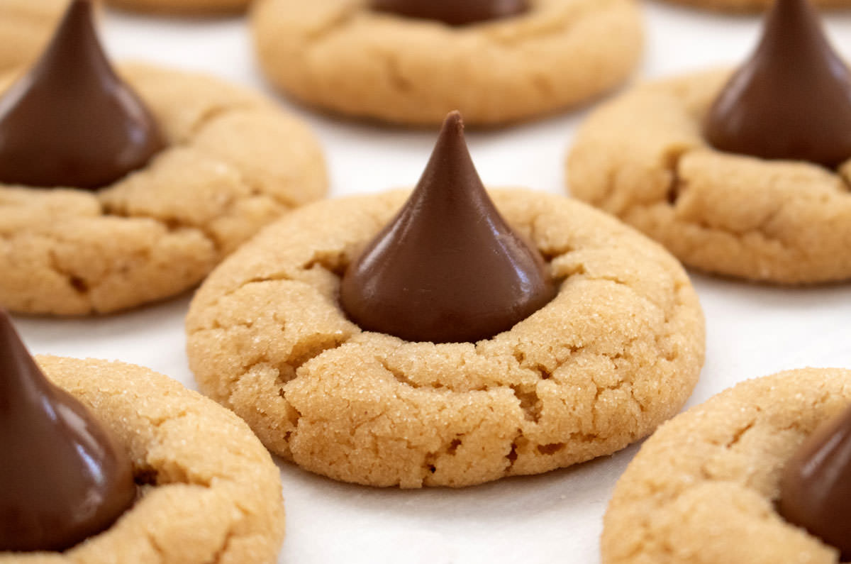 Closeup on a batch of Peanut Butter Blossoms sitting on a cookie sheet just out of the oven.