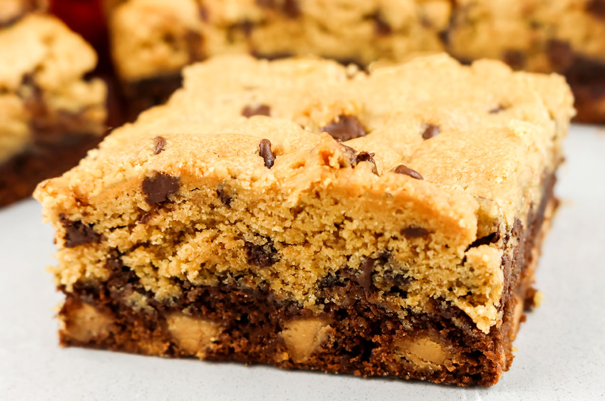 Closeup on a single Peanut Butter Brookie Bar sitting on a white surface in front of other bars.