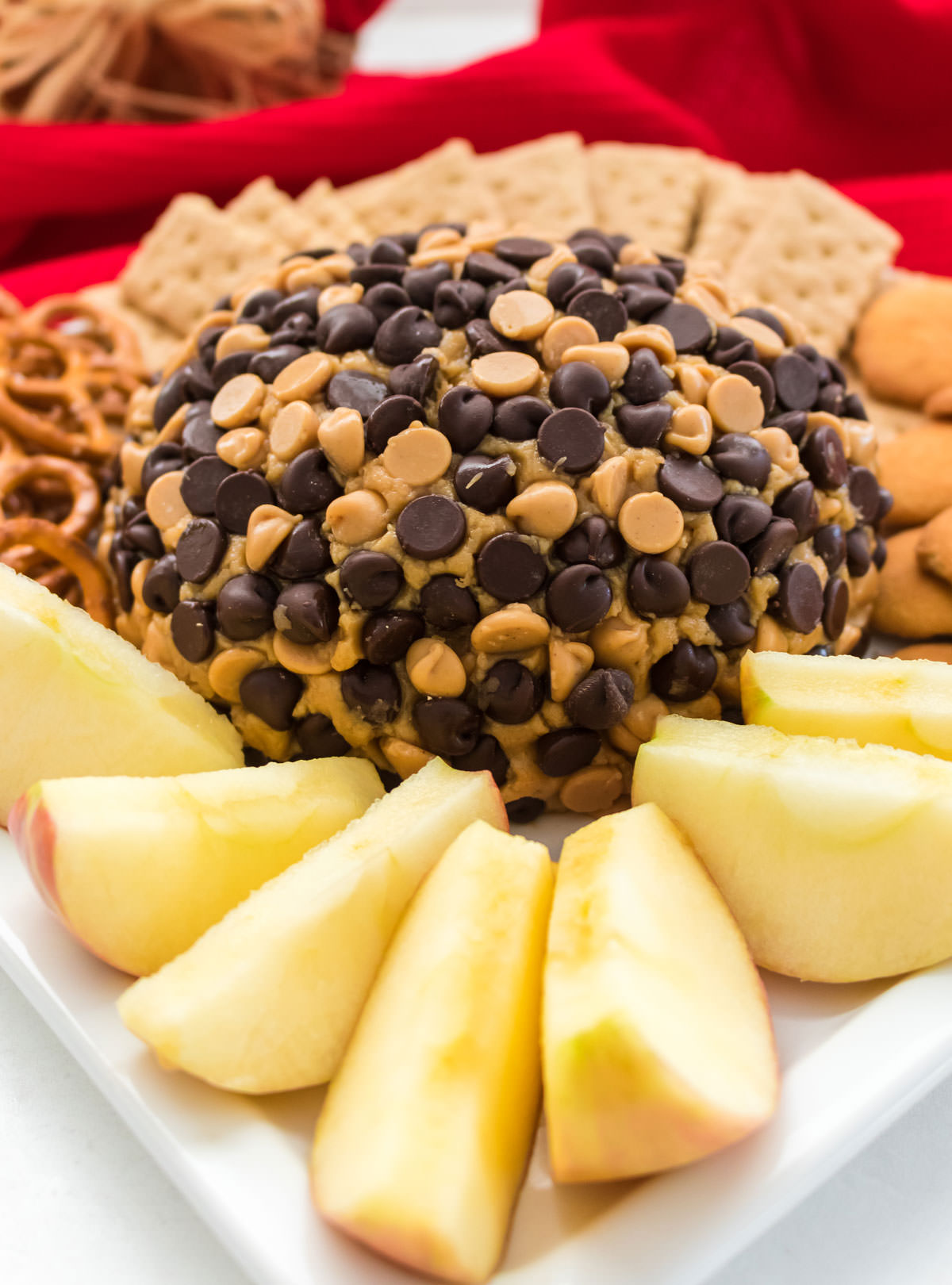 Peanut Butter Cheese Ball on a white plate surrounded by apple slices, pretzels, graham crackers and cookies.
