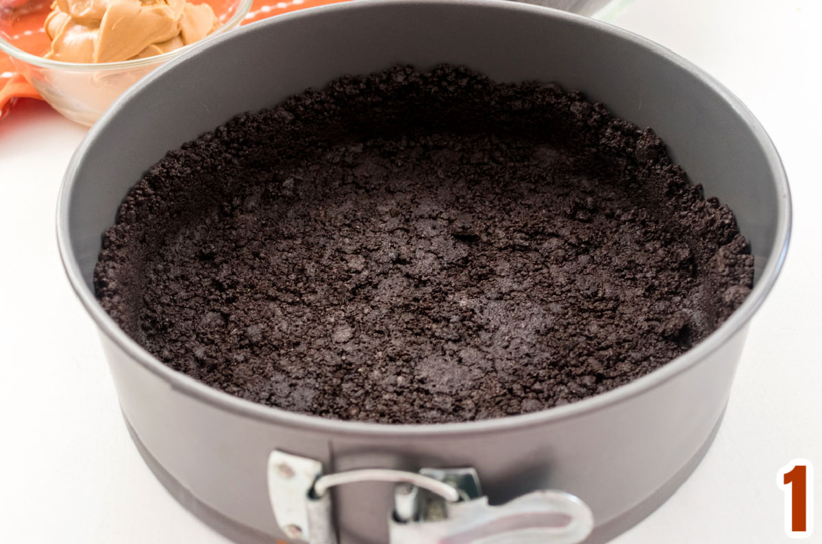 Closeup of an Oreo Cookie crust in a springform pan sitting on a white table.