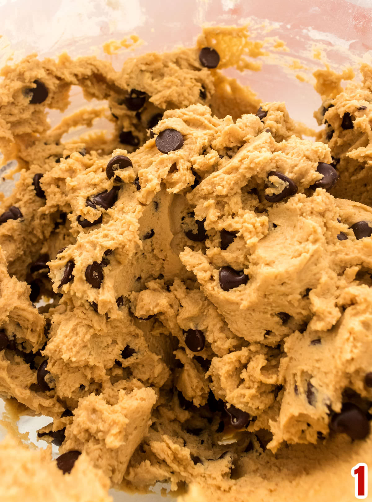 Closeup on a clear glass bowl filled with Peanut Butter Chocolate Chip cookie dough.