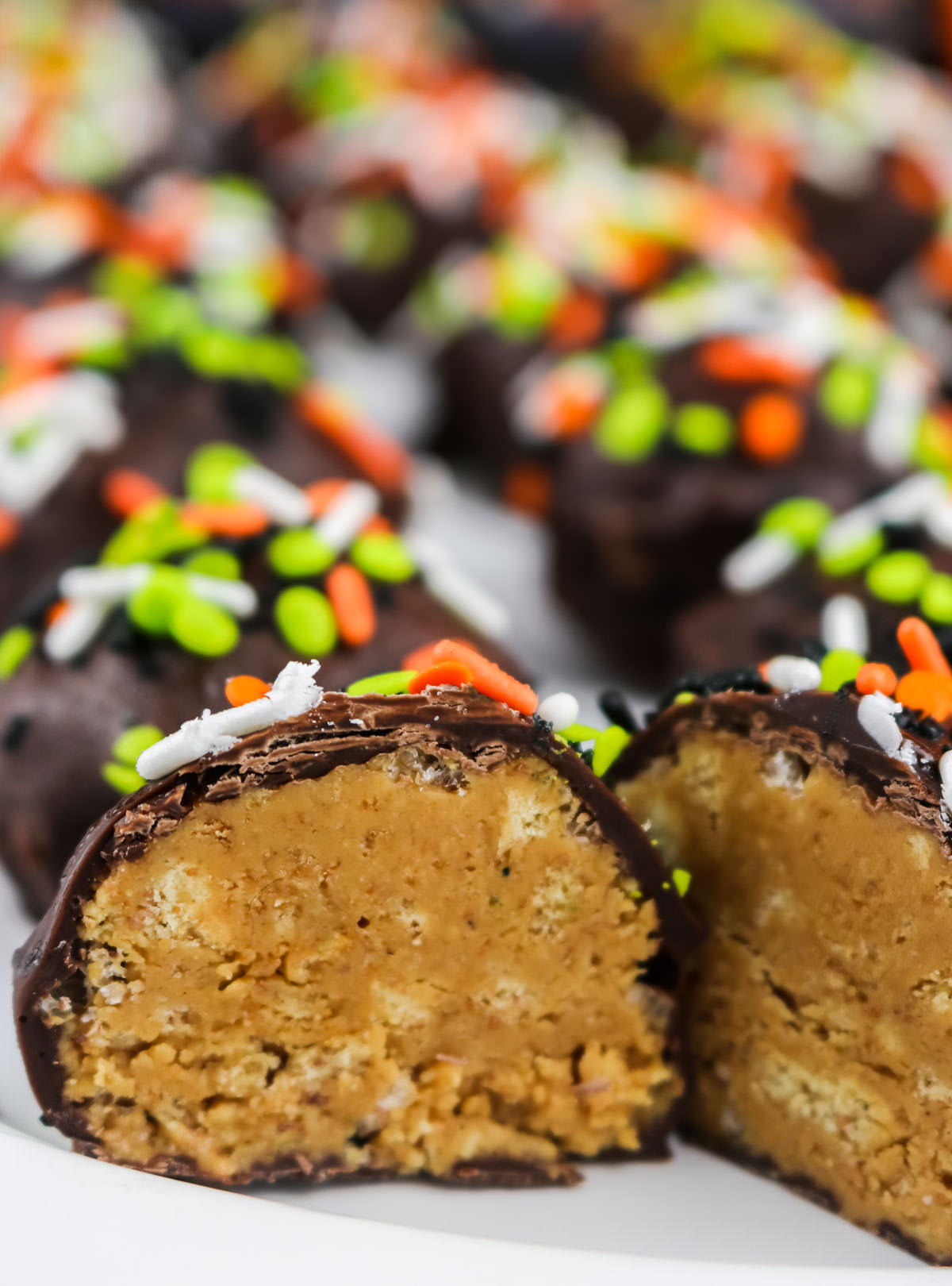 Closeup on a white serving platter holding a back of Peanut Butter Crunch Balls with the first one cut in half.