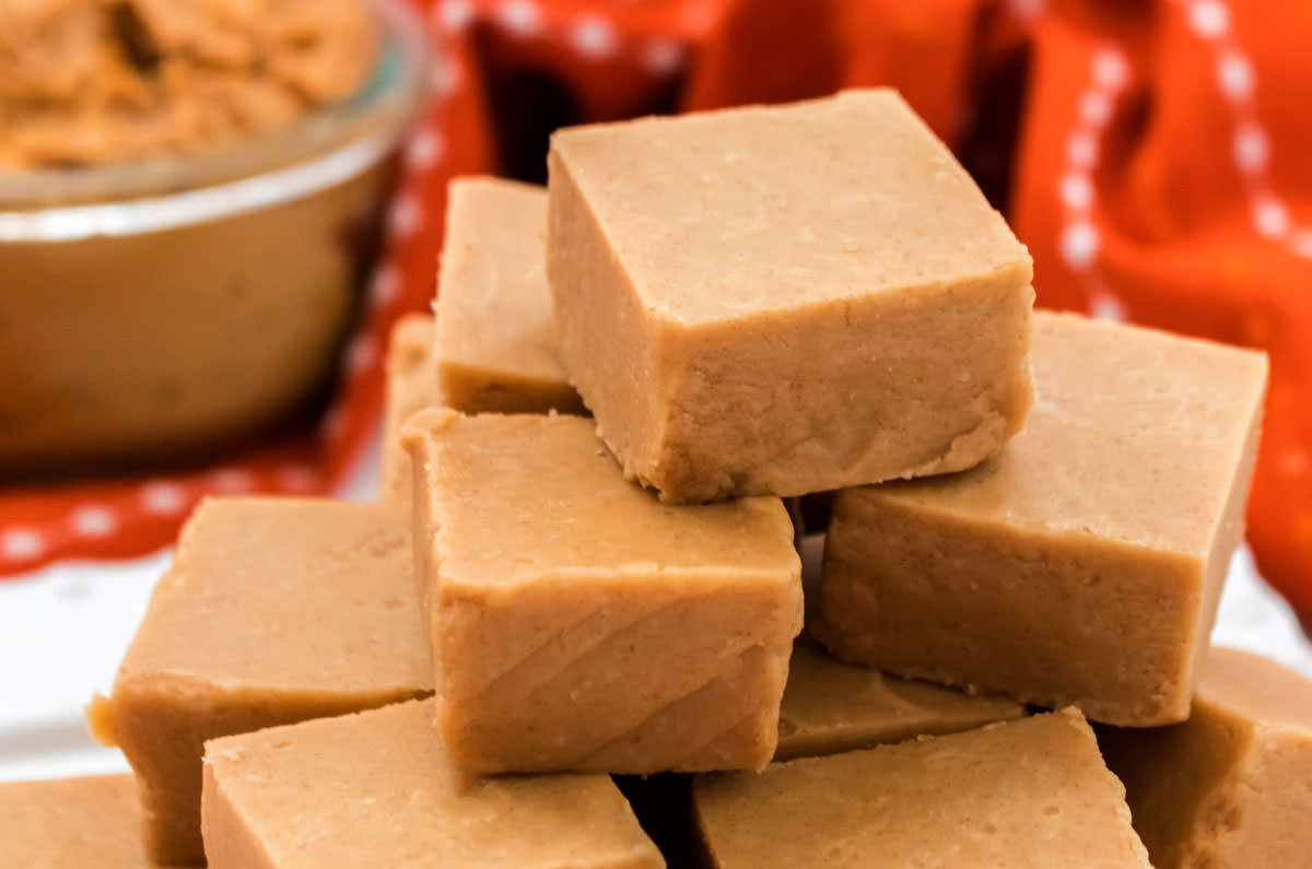 Stack of Peanut Butter Fudge sitting in front of a glass bowl filled with peanut butter.