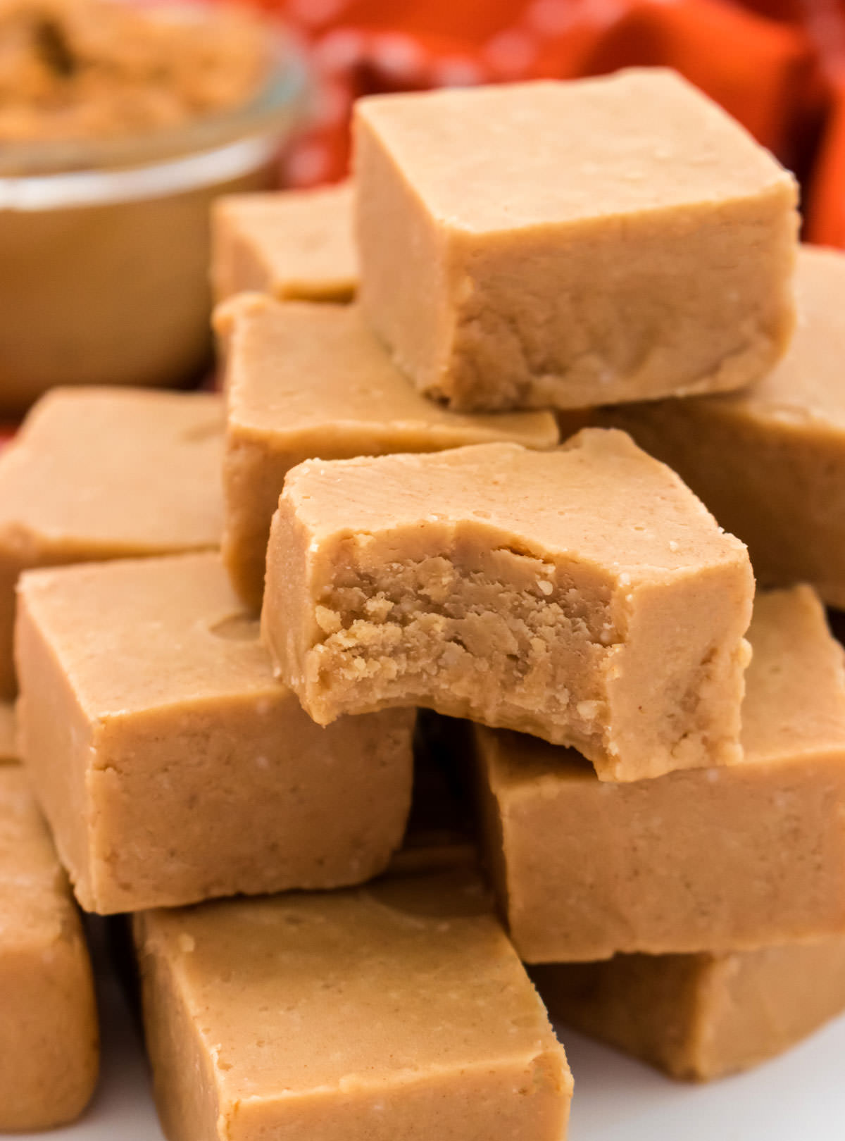 Closeup on a stack of Easy Peanut Butter Fudge sitting on a white surface, one piece with a bite taken out of it.