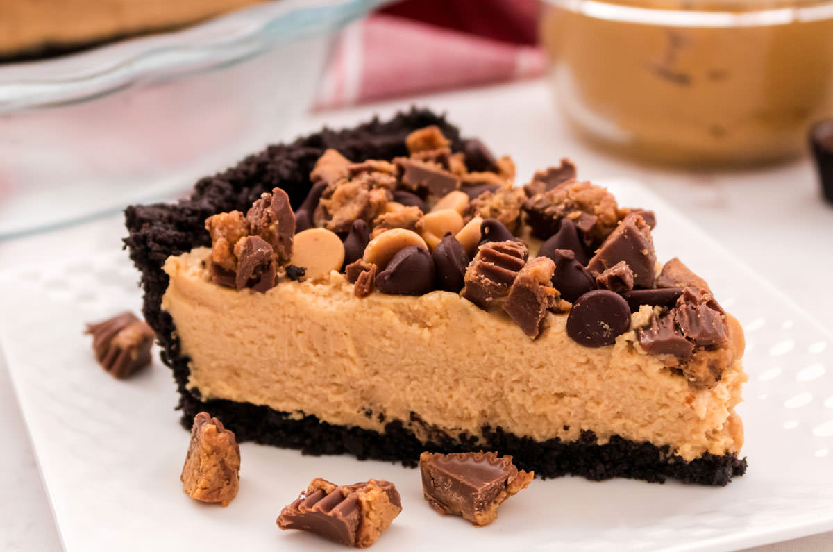 Closeup on a piece of Peanut Butter Pie sitting on a white plate with a glass bowl of Peanut Butter in the background.