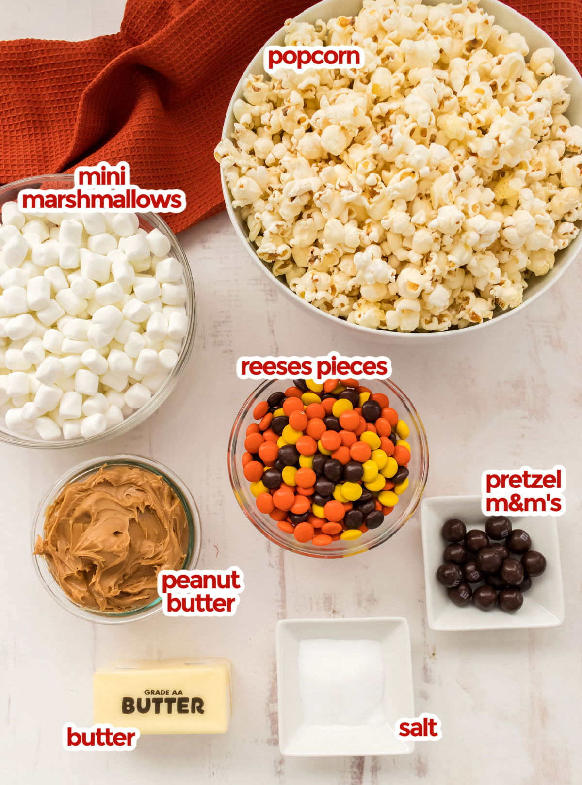 All the ingredients you will need to make Peanut Butter Popcorn including popcorn, mini marshmallows, peanut butter, butter, salt, Reese's Pieces and Pretzel M&M's.
