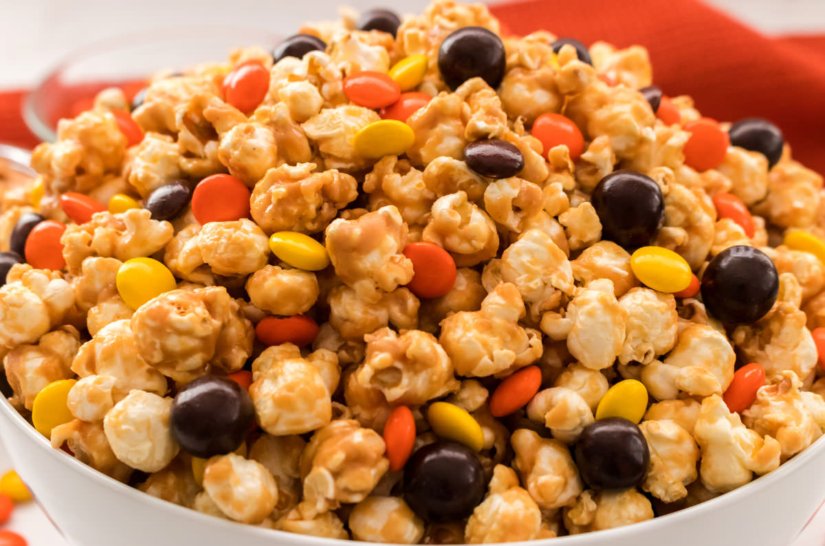 Closeup on a white serving bowl filled with Peanut Butter Popcorn that is topped with Reese's Pieces.