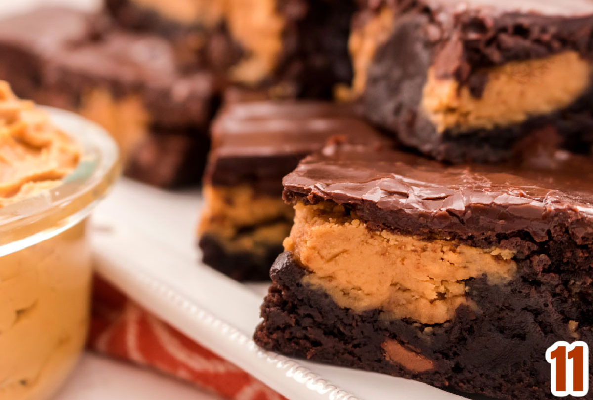 Closeup on a platter of Peanut Butter Swirl Brownies sitting next to a glass bowl filled with peanut butter.