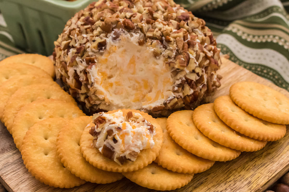 Pecan Cheese Ball sitting on a wooden cutting board with Ritz Crackers.
