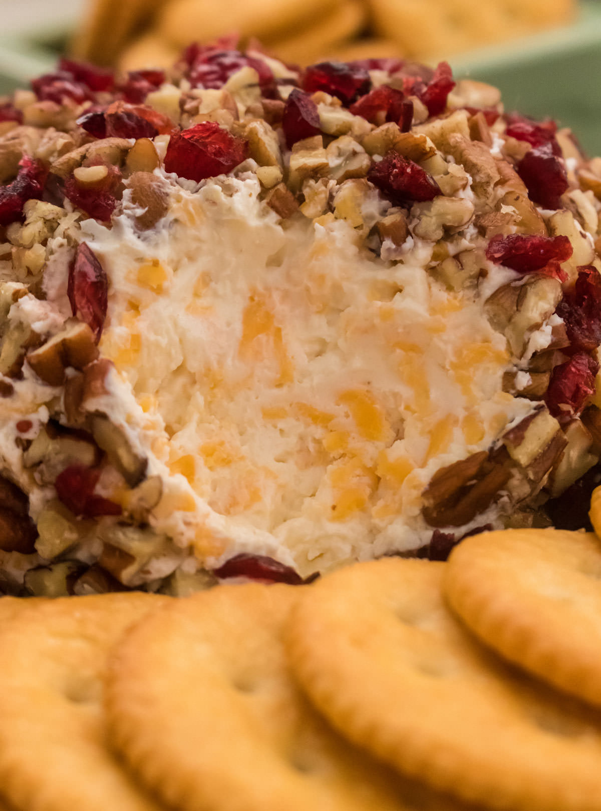 Cranberry Pecan Cheese Ball with the cheese mixture showing sitting in front of a stack of crackers.