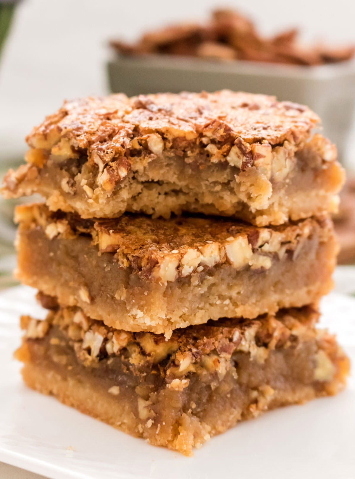 Closeup on a stack of three Pecan Pie Bars sitting on a white plate, the top one has a bite taken out of it.