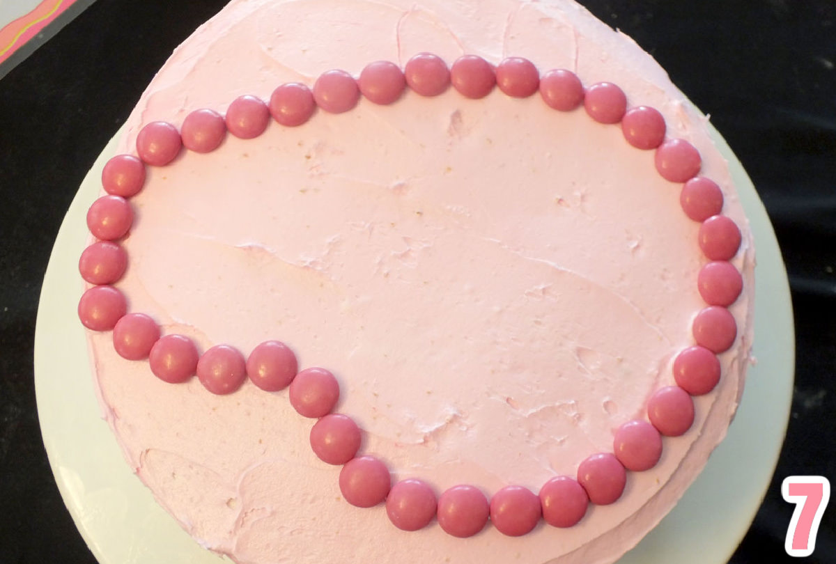 Closeup on the top of a cake frosted pink with the outline of Peppa Pig's face made with Pink M&M's.