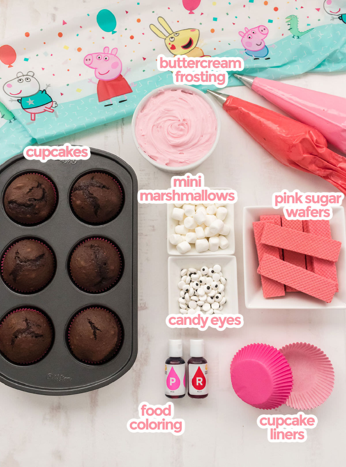 All the ingredients you will need to make Peppa Pig Cupcakes including cupcakes, buttercream frosting, food coloring, pink sugar wafers, mini marshmallows, candy eyes and cupcake liners.