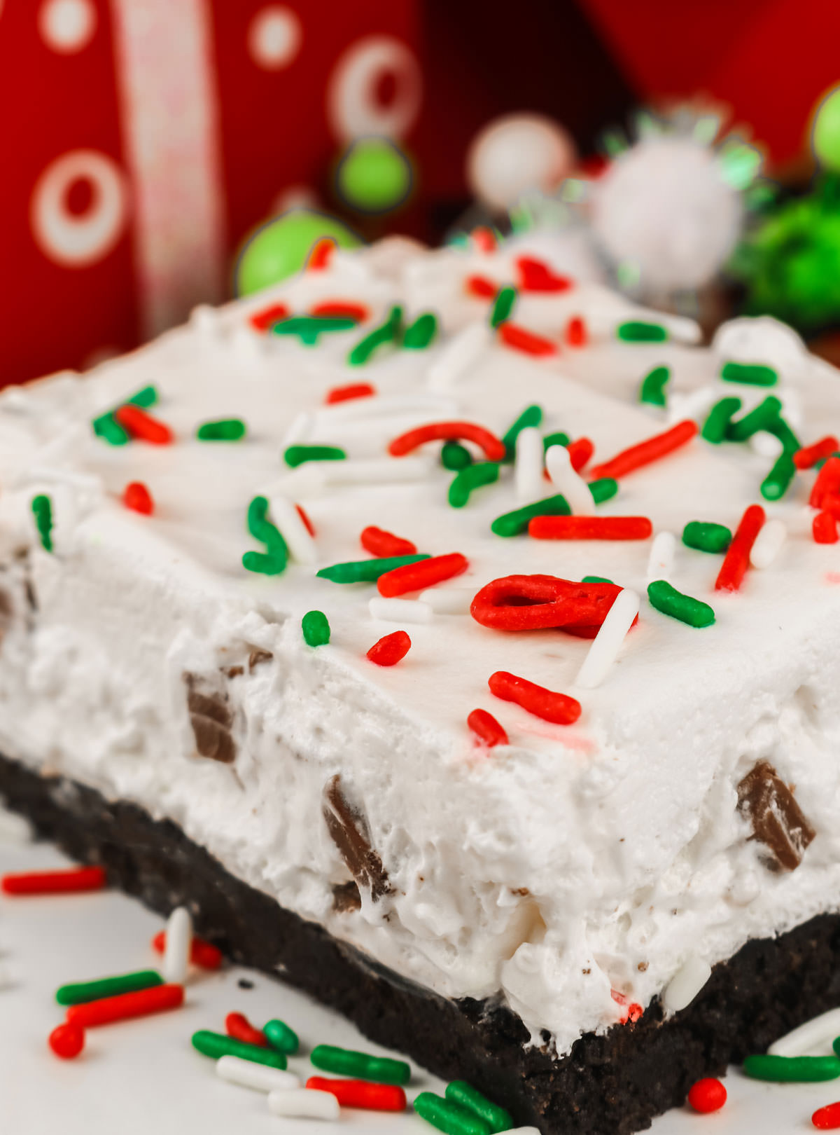 Closeup of a single piece of Peppermint Marshmallow No-Bake Dessert sitting on a white plate surrounded by Christmas sprinkles.